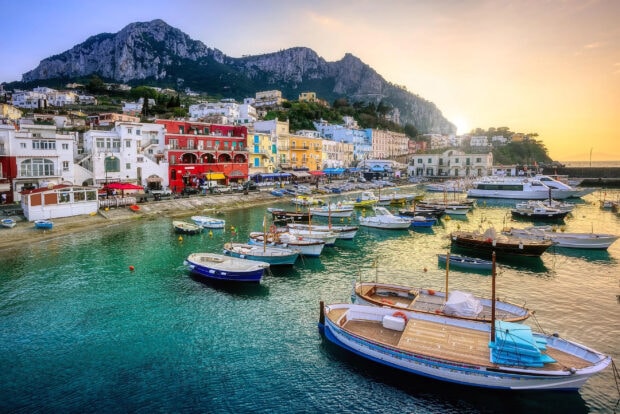Colorful buildings and boats at the harbor of Capri Island surrounded by mountains at sunset