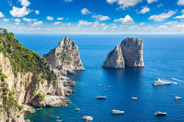 Stunning Capri Island cliffs with boats sailing on the vibrant blue sea under a clear sky