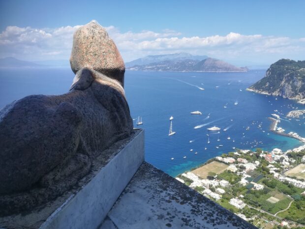 A granite statue overlooking the sea and boats on Capri Island coastline