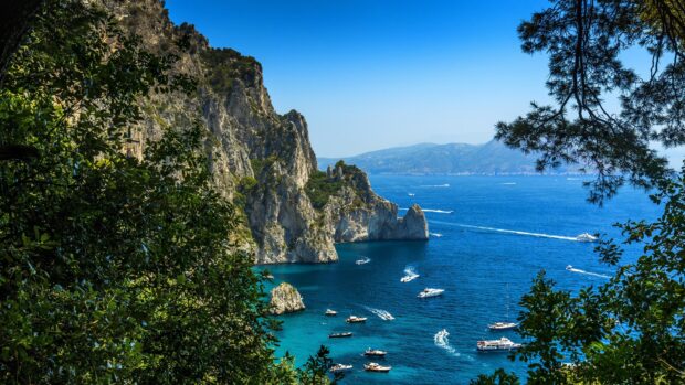 Beautiful Capri Island cliffs and boats on the clear blue sea surrounded by lush greenery