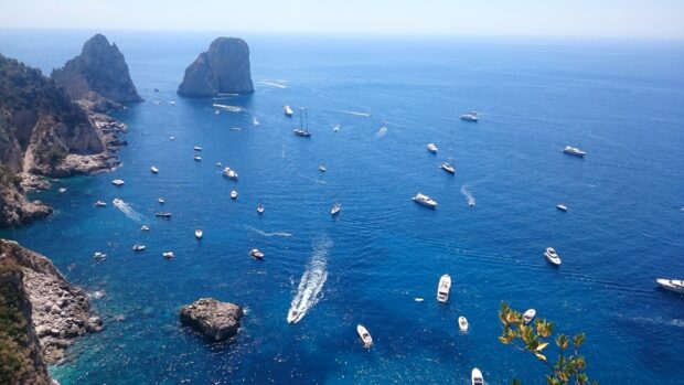 Aerial view of Capri Island with boats sailing on deep blue sea and rocky cliffs around