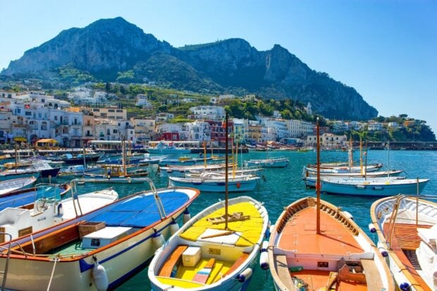 Colorful boats docked at Capri Island harbor with scenic mountain view in clear daylight