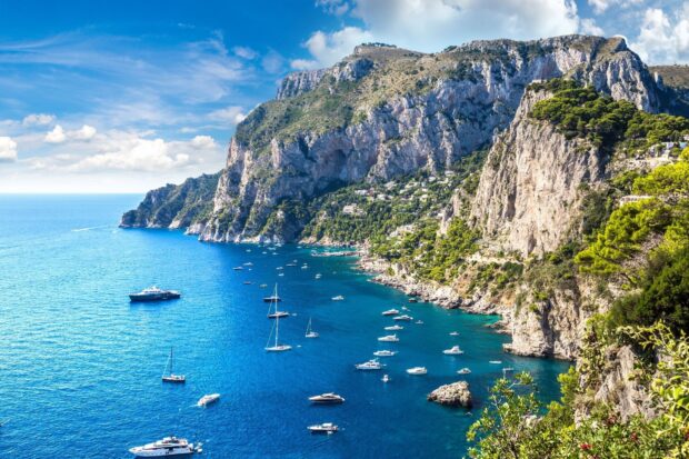 Stunning view of Capri Island with boats sailing along the blue sea near rocky cliffs