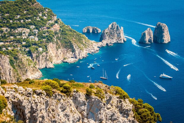 A scenic view of Capri Island with rocky cliffs and boats sailing in the blue sea
