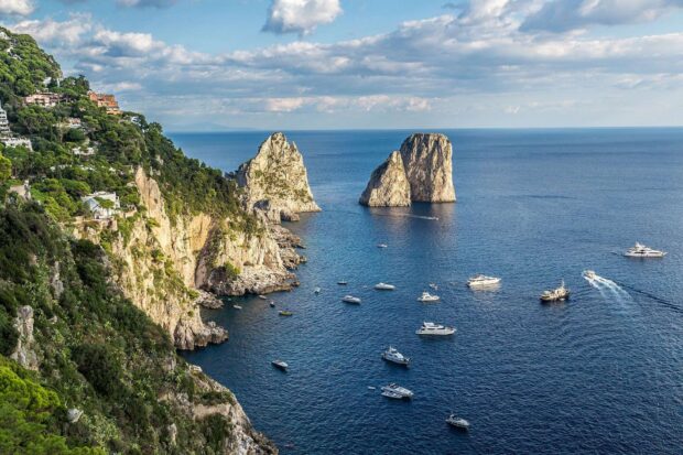 The Capri Island coastline with boats sailing on the blue sea under a cloudy sky