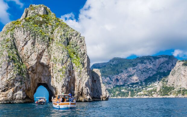 Tourists on a boat exploring the natural rock arch on Capri Island with clear blue sky and sea