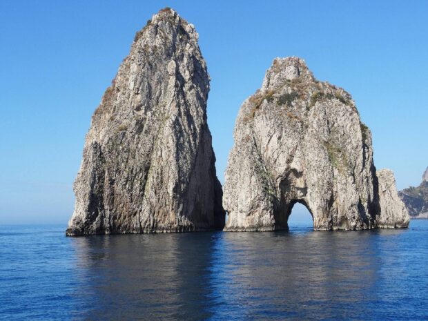 Two large rock formations of Capri Island rise above calm blue sea water