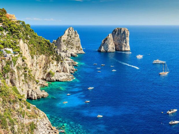 A stunning view of Capri Island cliffs and azure sea with boats in clear blue water