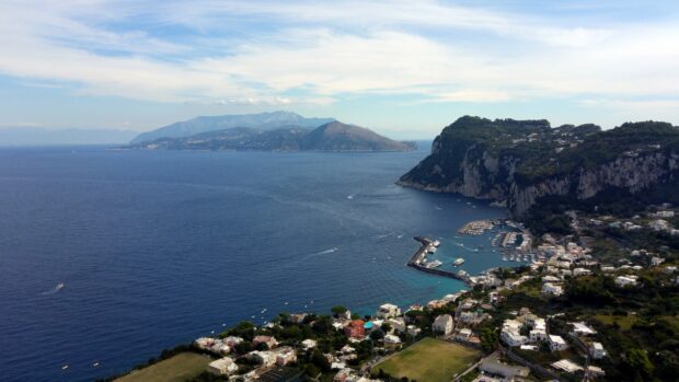 Aerial view of Capri Island coastline with boats and buildings under a cloudy sky