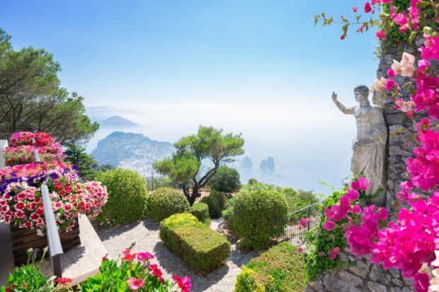 Beautiful Capri Island garden with vibrant flowers and ancient statue overlooking the sea