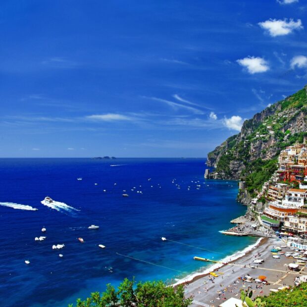 Capri Island coastline with clear blue sea and boats near the colorful hillside buildings