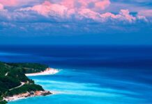 Tropical Caribbean Islands coast with clear blue water and lush green trees under pink clouds