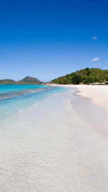 Clear turquoise water along the Caribbean Islands pristine shore with green hills in the background