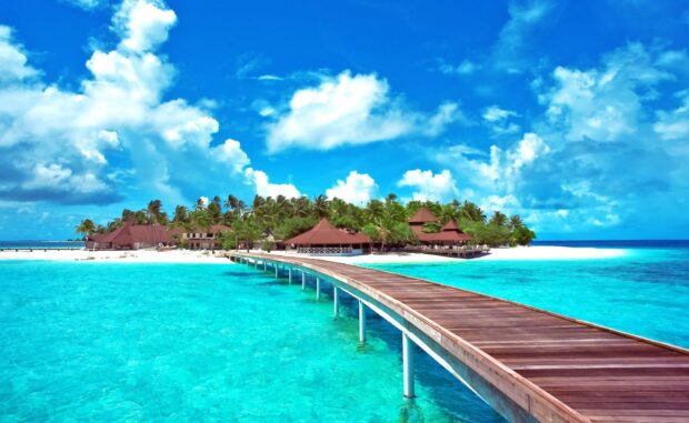 A wooden pier leading to a tropical Caribbean islands with clear turquoise water and palm trees