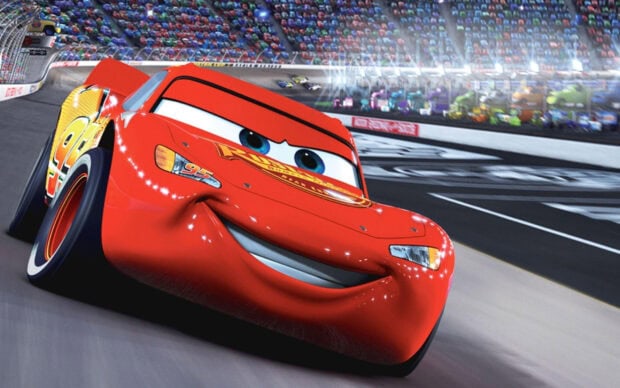 Red animated character from Cars Disney racing on the track in a stadium full of cars