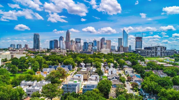 A vibrant view of the Charlotte city skyline with lush greenery and modern buildings under a partly cloudy sky