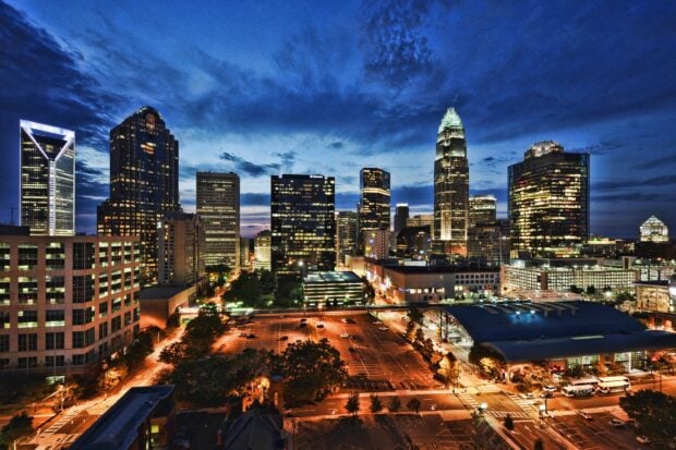 The Charlotte skyline at dusk with illuminated skyscrapers and a vibrant cityscape