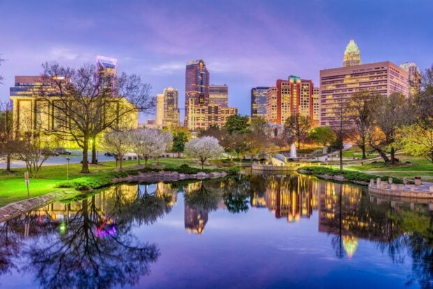 Charlotte cityscape featuring skyscrapers reflecting in calm park water during twilight