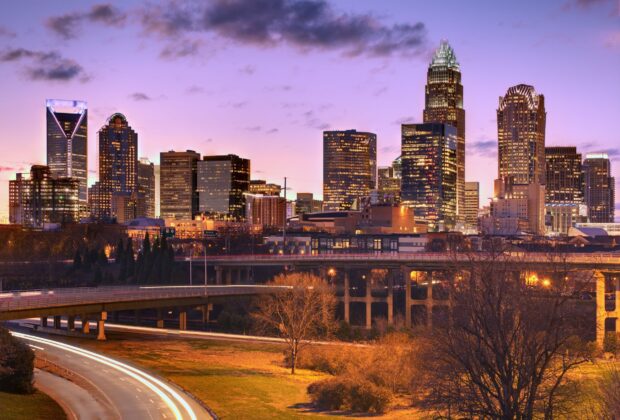 Charlotte skyline at dusk with illuminated buildings and a clear purple sky