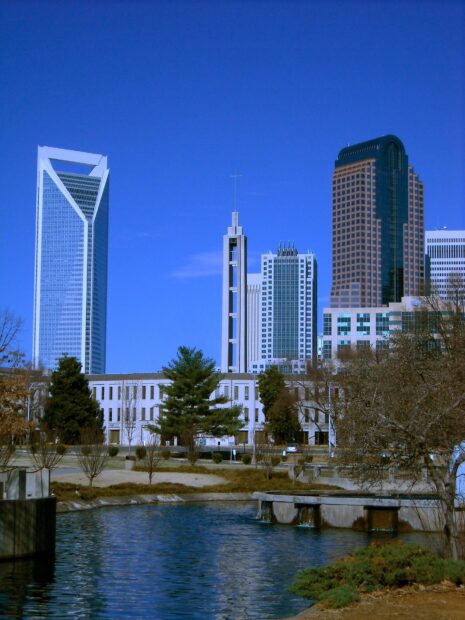 The Charlotte skyline features modern skyscrapers and a clear blue sky with a peaceful river in the foreground