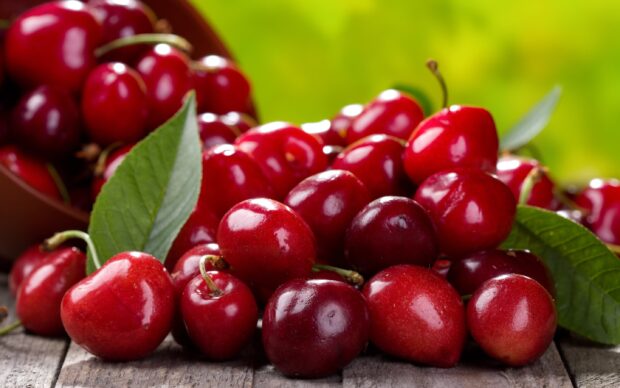 Fresh red cherry fruit close up with green leaves on wooden table