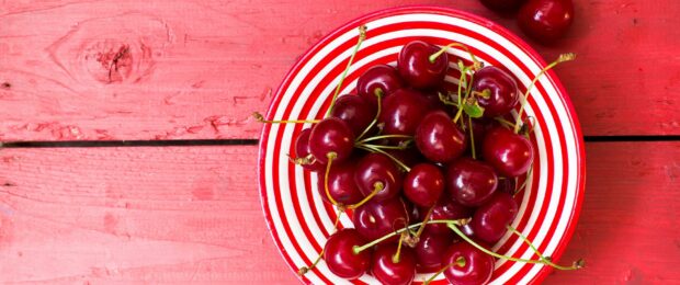 Fresh ripe cherry fruits in a bowl on a red wooden surface