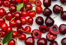 A close up view of fresh red and dark cherry fruits with green leaves on a white surface