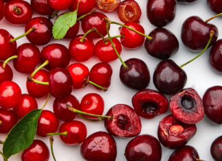 A close up view of fresh red and dark cherry fruits with green leaves on a white surface