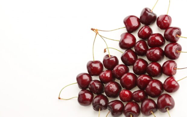 Fresh ripe cherry fruits with stems scattered on a white surface