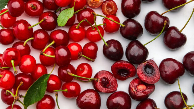 A close up view of fresh red and dark cherry fruits with green leaves on a white surface