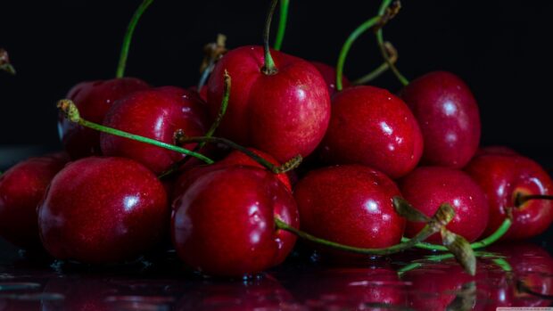 Fresh red cherry fruits piled together on a reflective surface with dark background