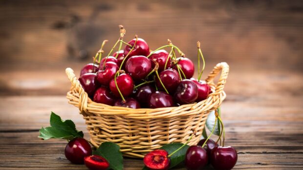 A basket full of fresh cherry with leaves on wooden table