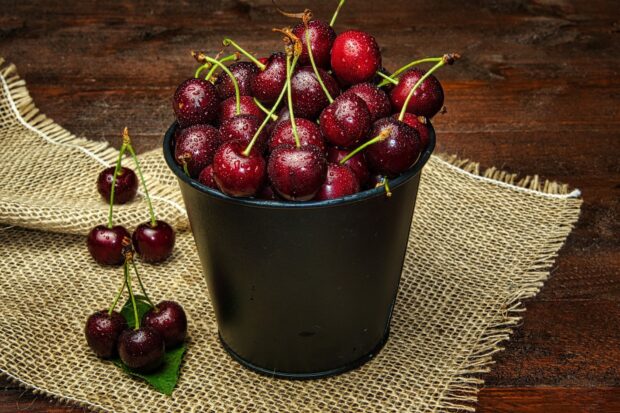 Fresh cherries with stems in a black container on burlap and wooden surface