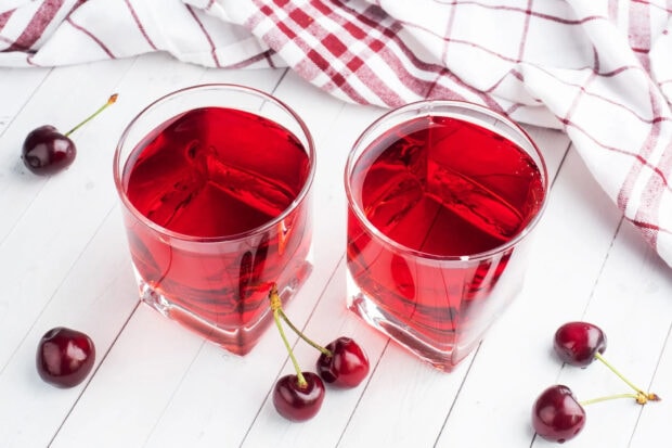 Two glasses of red cherry drink with fresh cherries on white wooden table