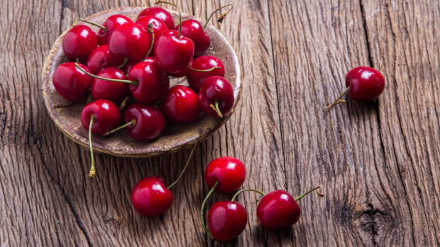 A bowl of fresh cherries on a rustic wooden surface with scattered cherries around