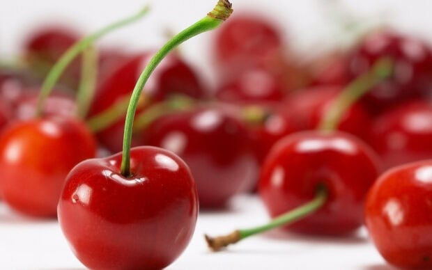 A close up of fresh cherry with a green stem on a white surface surrounded by other cherries