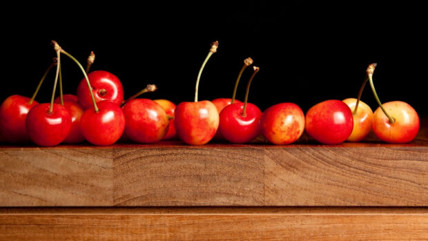 A row of fresh cherry fruits with stems placed on a wooden surface against a black background