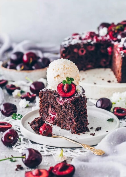 A slice of chocolate cake with fresh cherry pieces and a scoop of ice cream on top