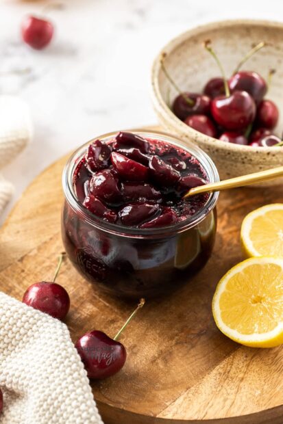 A close up of cherry fruit preserves with fresh cherries and lemon on wooden board