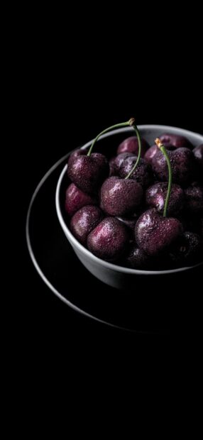 Fresh ripe cherries with water droplets in a bowl on a black background