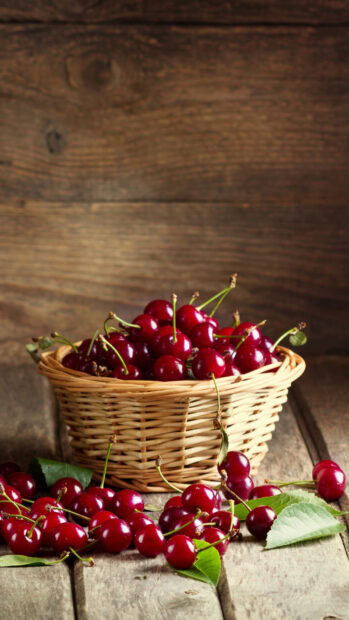 Fresh ripe cherry fruits in a wicker basket with green leaves on wooden surface