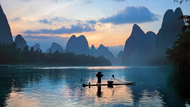 A serene riverscape with traditional Chinese fisherman and karst mountains at sunset in China