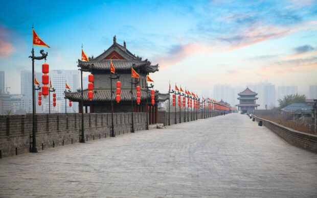 Ancient China architecture along city wall with red lanterns and flags on a clear sky background