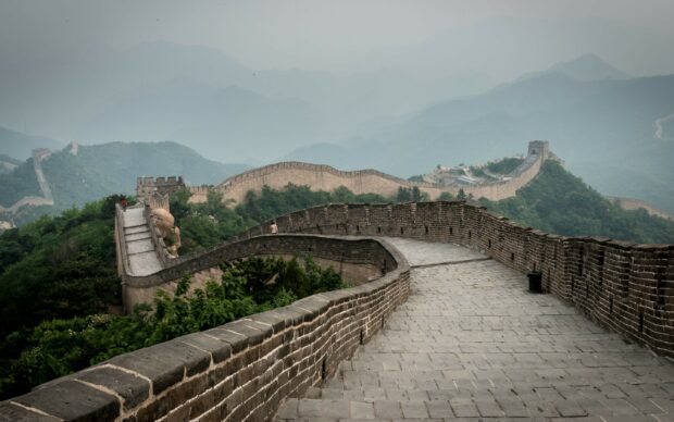 The Great Wall of China stretches over green hills under a hazy sky in China