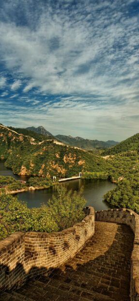 Ancient China landscape showing lush mountains and a historic wall near a river