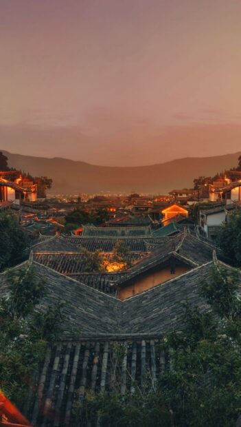 Traditional China town rooftops glowing warmly at sunset with mountain backdrop