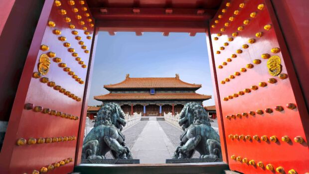 Traditional Chinese architecture framed by red doors and guardian lion statues at a historic site in China