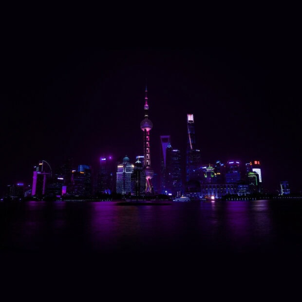 Neon lights illuminate the Shanghai skyline at night with iconic landmarks glowing purple