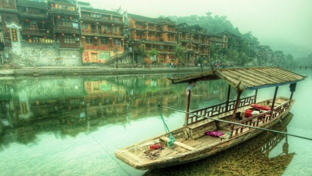 Traditional China boat floating on river with ancient buildings in background