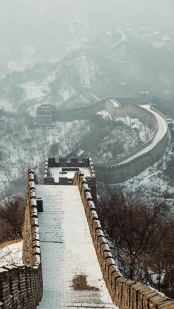 Snow covered sections of the Great Wall of China winding through misty mountains in winter